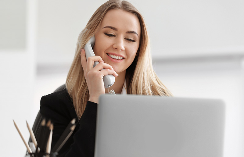 Woman talking on office phone and using laptop